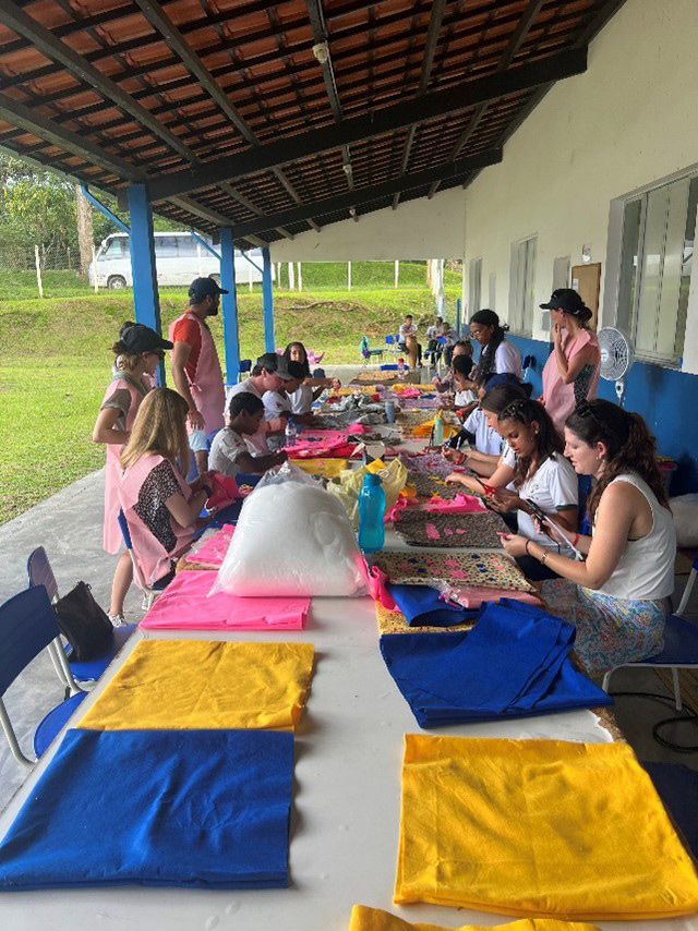 students and children sitting at a long table working with bright fabric